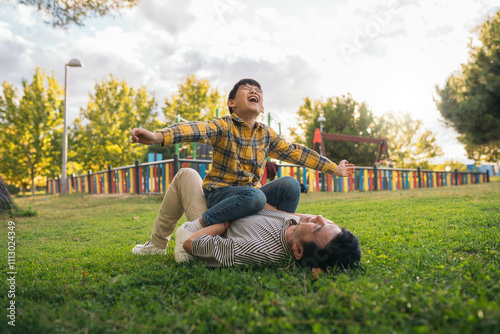 Child laughing while sitting on parent lying in the park photo