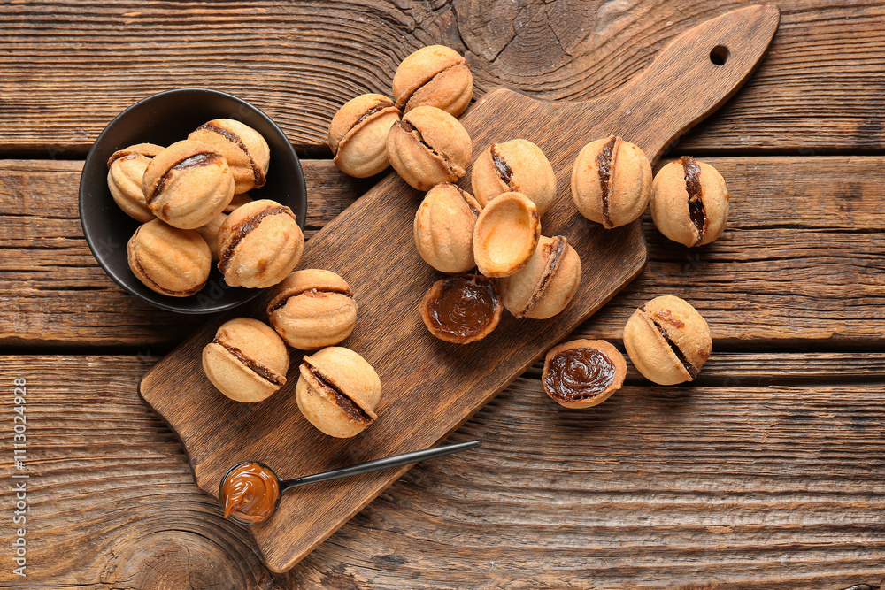 Bowl and cutting board of sweet walnut shaped cookies with boiled condensed milk on wooden background Bowl and cutting board of sweet walnut shaped cookies with boiled condensed milk on wooden background