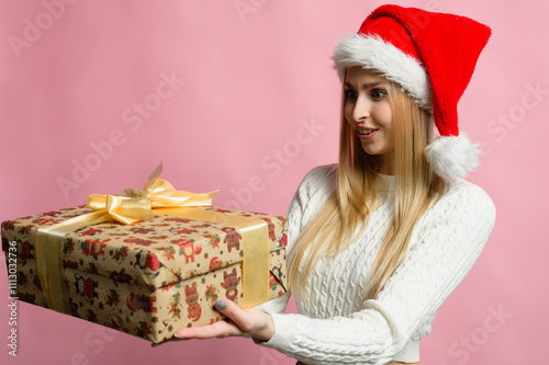 Smiling woman in Christmas hat with wrapped gifts in front of pink background.