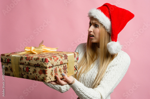 Smiling woman in Christmas hat with wrapped gifts in front of pink background.