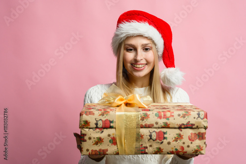 Smiling woman in Christmas hat with wrapped gifts in front of pink background.