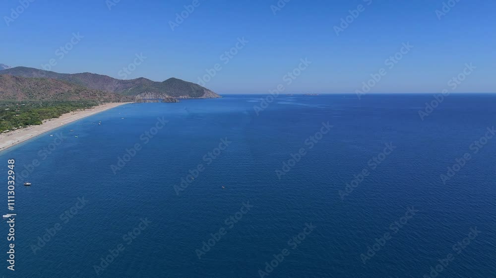 Aerial drone view showcasing a crowded beach and the rugged, rocky mountains of Turkey on a sunny day by the sea.