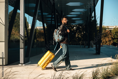 An Indian man comes out of the building with a yellow suitcase. photo