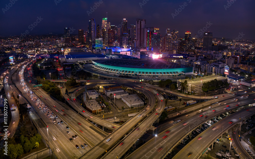 Fototapeta premium JANUARY 2024, LOS ANGELES, CA. - aerial view of LA Skyline & Convention Center at dusk showing intersection of Harbor Freeway 110 and Interstate Highway 10 with traffic