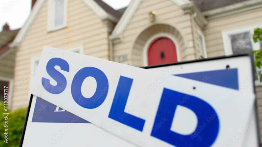 Sold house sign in front of a beige house with a red door. Sold house sign in front of a beige house with a red door.
