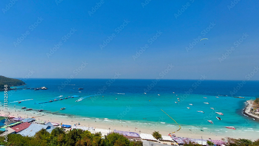 Tourists enjoying parasailing and speedboats in beautiful turquoise ocean water at a tropical island beach resort Tourists enjoying parasailing and speedboats in beautiful turquoise ocean water at a tropical island beach resort