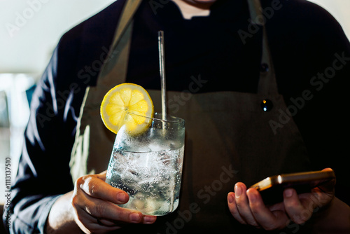 Person holding a drink with lemon garnish and a smartphone photo