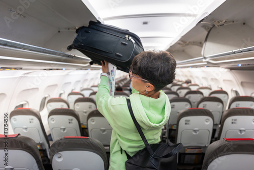 Woman placing luggage in overhead compartment on airplane photo