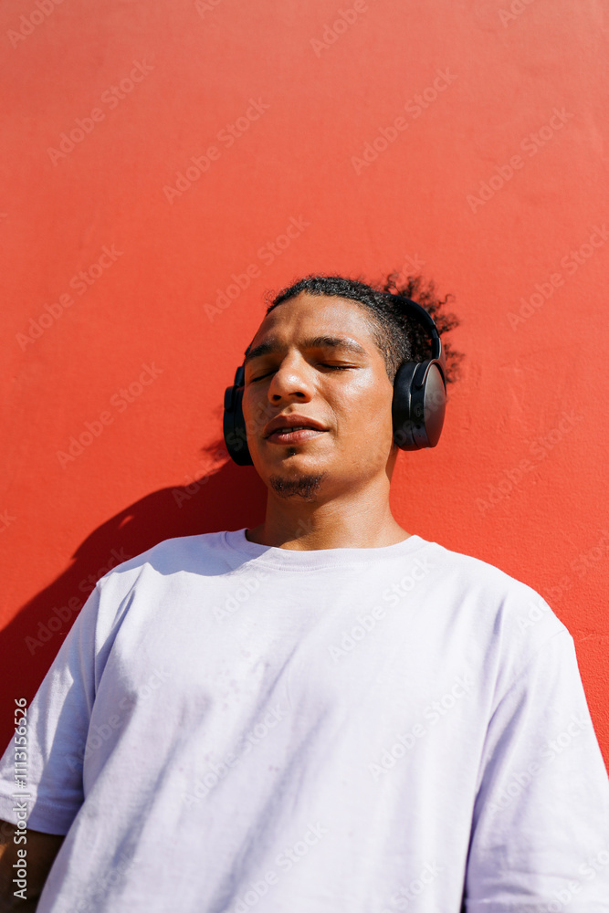 © Artem Podrez/Stocksy - Relaxed Man Listening to Music Outdoors Against Red Wall © Artem Podrez/Stocksy - Relaxed Man Listening to Music Outdoors Against Red Wall