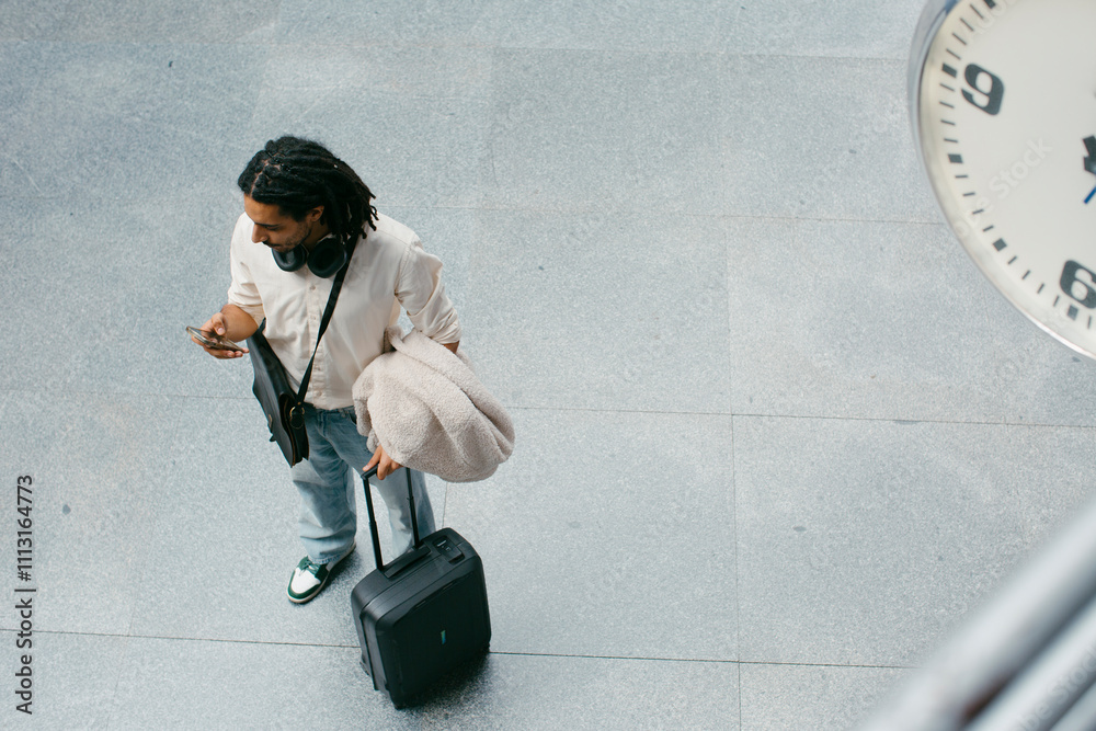Traveling man with carry-on suitcase checking phone in station Traveling man with carry-on suitcase checking phone in station