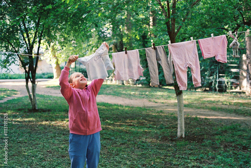 Smiling cheerful girl hanging out washed baby clothes on the street. photo