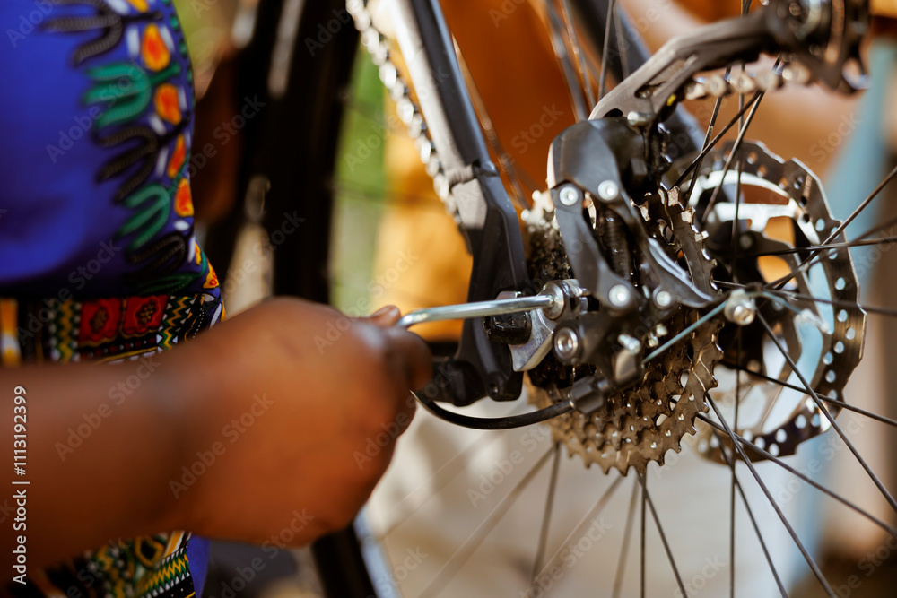 Obraz premium African american female hand using equipment to repair damaged bicycle chain ring outdoors. Closeup of person adjusting bike derailleur with professional tool in home yard.