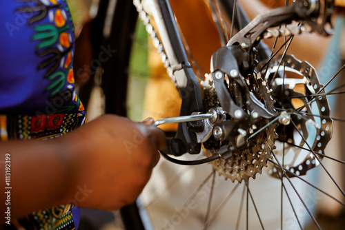 African american female hand using equipment to repair damaged bicycle chain ring outdoors. Closeup of person adjusting bike derailleur with professional tool in home yard. photo