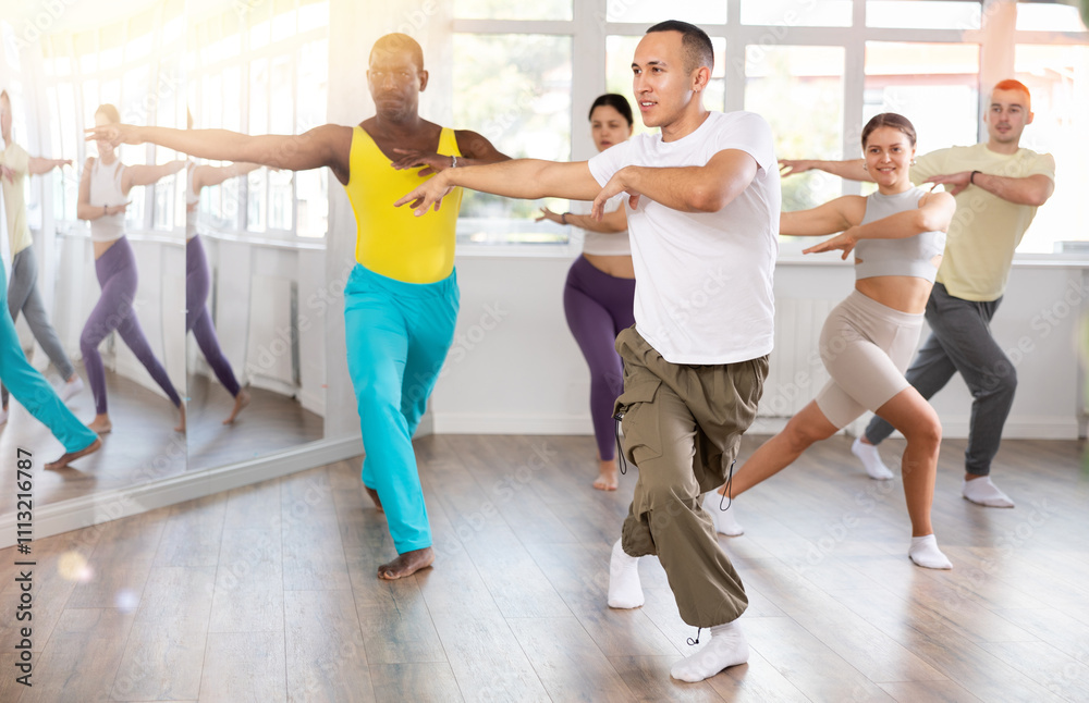 Fototapeta premium During dance workshop, European guy with team of like-minded multinational people learn to perform elements of energy waacking dance. Studio school for amateur and professional dancers