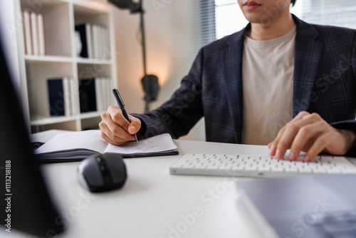 Businessman writing in diary while using computer at desk photo
