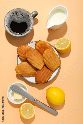 Madeleine cakes, milk jug, cup of coffee, lemon and butter on orange background, top view photo