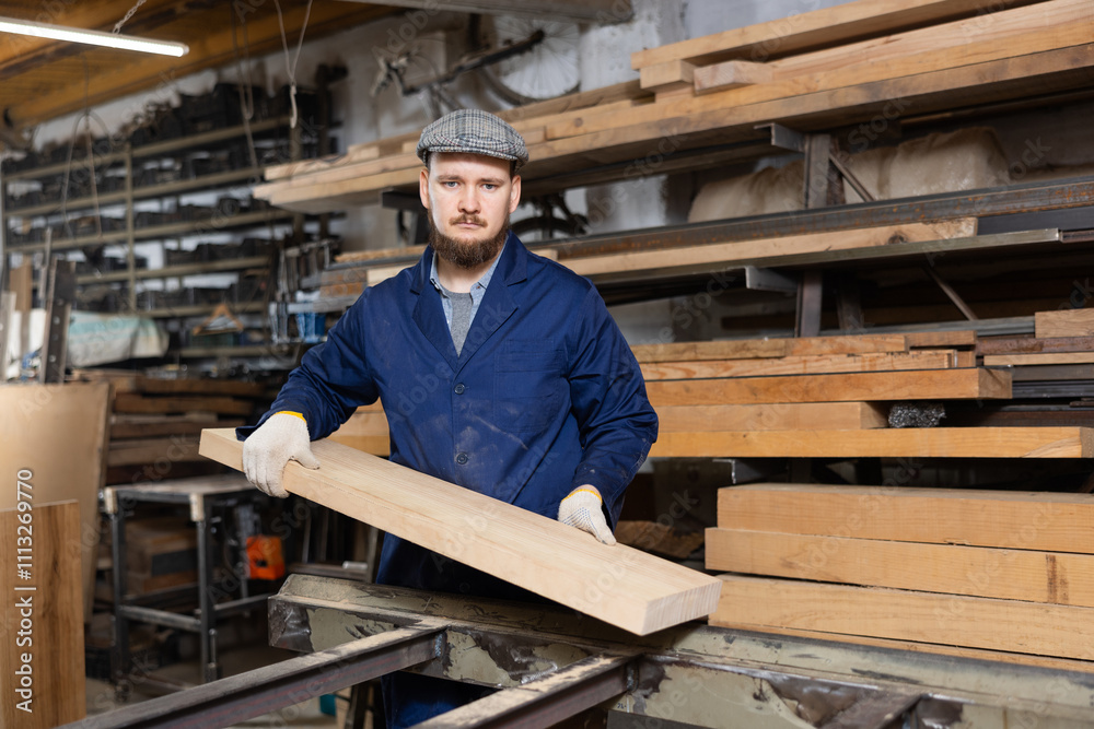 Male worker in uniform carries board from storage location to processing location. Selects planks for furniture manufacture Male worker in uniform carries board from storage location to processing location. Selects planks for furniture manufacture