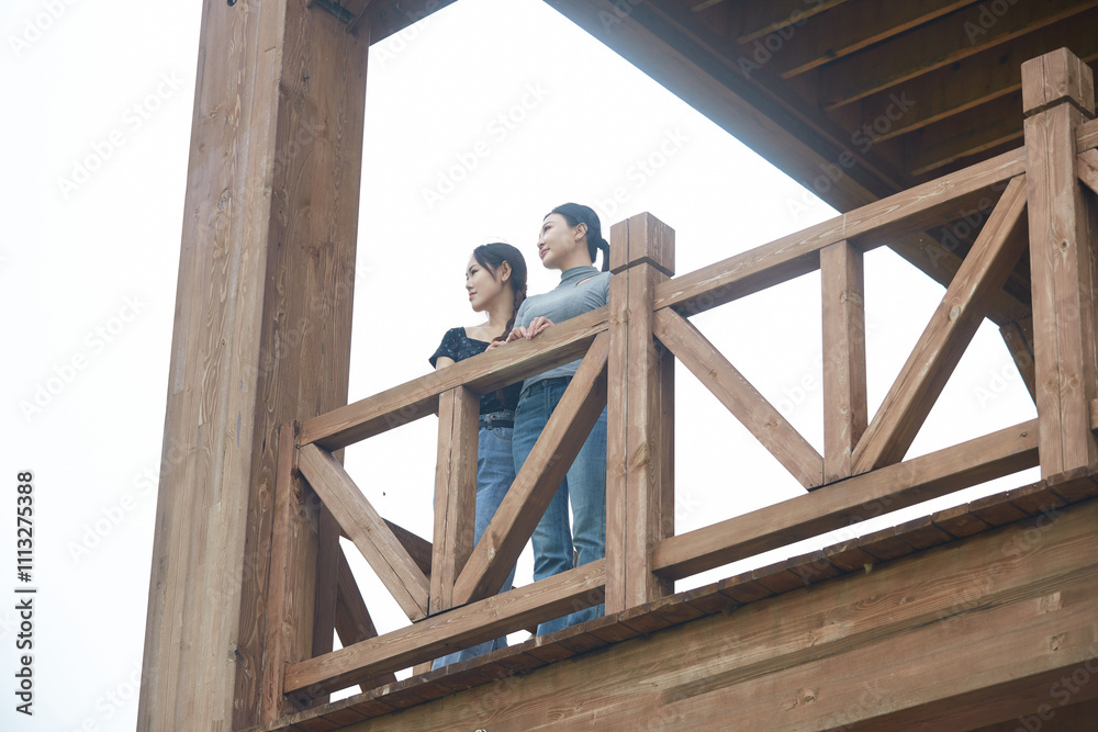 Beautiful girlfriends taking photos and playing at the bird watching platform in the grassland flower sea