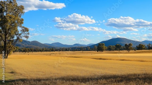 A serene landscape featuring golden fields, distant mountains, and a clear blue sky.