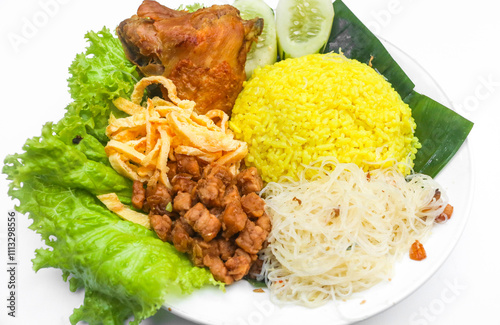 Yellow rice with side dishes of chicken, tempeh, scrambled eggs, noodles and chili sauce is served on a plate. Indonesian style yellow rice photo