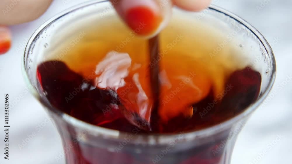 A hand is gently stirring a warm drink in a transparent and clear glass container. A hand is gently stirring a warm drink in a transparent and clear glass container.