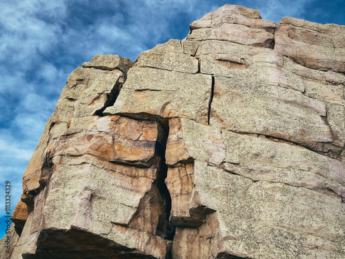 A massive boulder with prominent cracks running through its surface, set against a vibrant blue sky with scattered clouds. The rock's rugged texture and earthy tones highlight its natural beauty photo