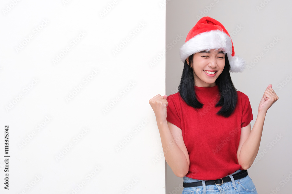 A woman wearing santa christmas hat leaning on the wall showing excited expression A woman wearing santa christmas hat leaning on the wall showing excited expression