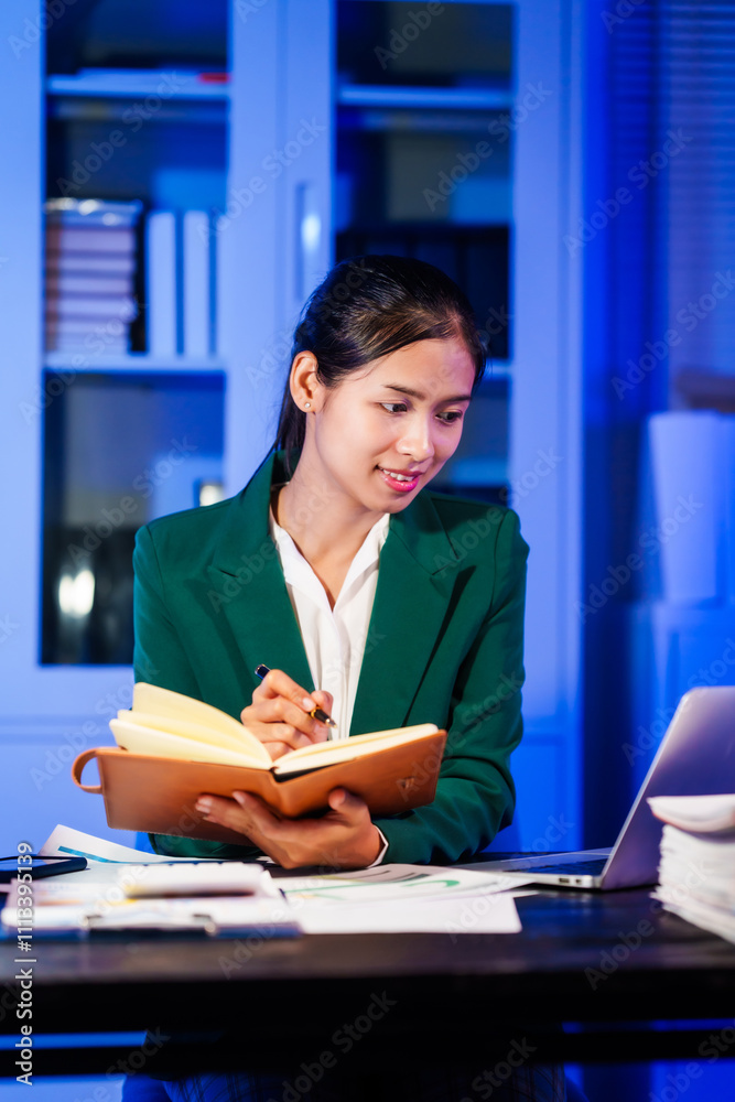 An Asian businesswoman works overtime,sitting at her desk at night, searching through numerous documents on her PC or laptop.Facing office problems,she also chats online while handling lots of work
