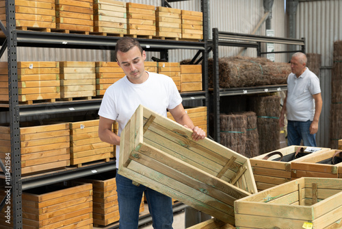 Male customer chooses wooden box in store. Man inspects wooden box for storing garden equipment.