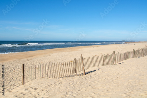 Detail of a light wooden railing made of sticks placed on the white sand of a beach and netx to de sea at Costa Nova in Aveiro, Portugal. photo