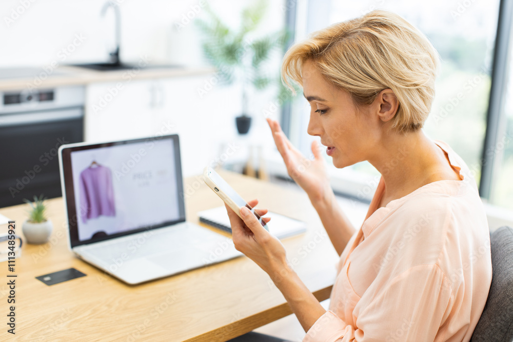 © sofiko14 - Caucasian adult woman expressing frustration while making phone call to discuss online clothing order issue. Her laptop shows purchased item confirming concern.