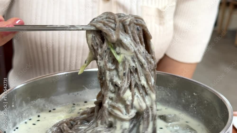 검은깨로 만든 면이 들어간 한국식 차가운 콩국수를 젓가락으로 들어올린 부드러운 움직임