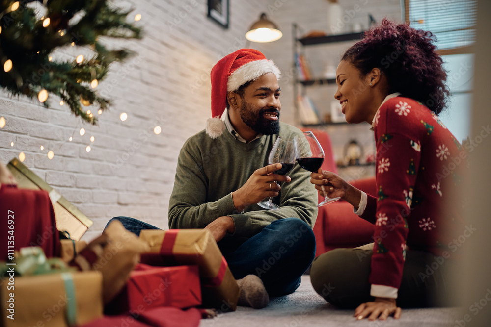 Fototapeta premium Smiling black couple toasting with wine while celebrating Christmas at home.