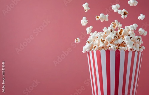 Freshly popped popcorn overflowing from a striped container on a pink background
