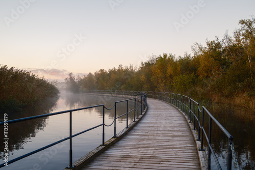 Floating bridge at Gentofte Lake early morning at dawn in autumn. Trees reflecting in the calm water.