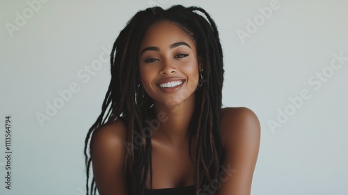Smiling woman with long dreadlocks poses against a plain background indoors