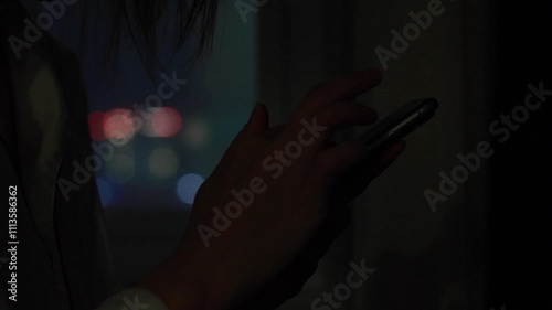 夜の暗い部屋でスマートフォンを見ている女性　窓から見える夜景　室内