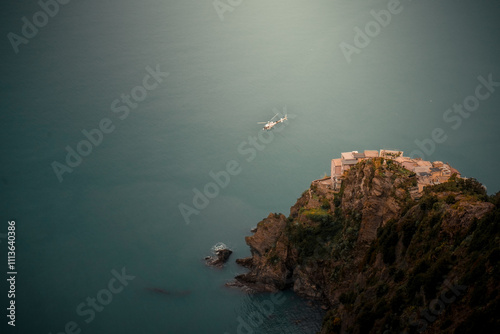 A captivating view of Manarola, one of the iconic villages of Cinque Terre, Italy. Vibrant houses are perched on a dramatic cliff overlooking the turquoise waters of the Ligurian Sea. The overcast sky