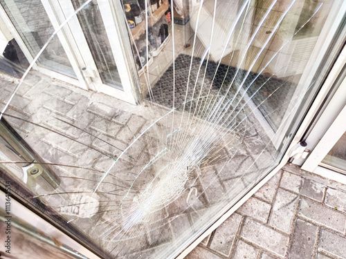 A close-up of a shattered glass door window with a spiderweb pattern of cracks