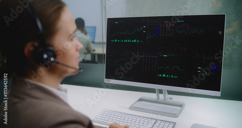 Professional female financial specialist talks on headset with investor, analyzes share market and stocks on computer. PC screen shows charts and diagrams. Stock exchange company office. E-business.