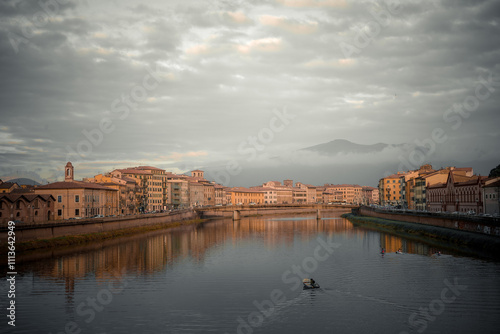 Wallpaper Mural A serene riverside view in Pisa, Italy, during sunset. The warm light highlights the historic buildings with their traditional architecture, while the calm river reflects the soft colors of the sky.  Torontodigital.ca