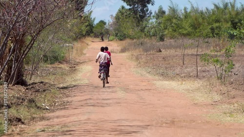 Two figures riding bicycles down a dirt road in a remote African village