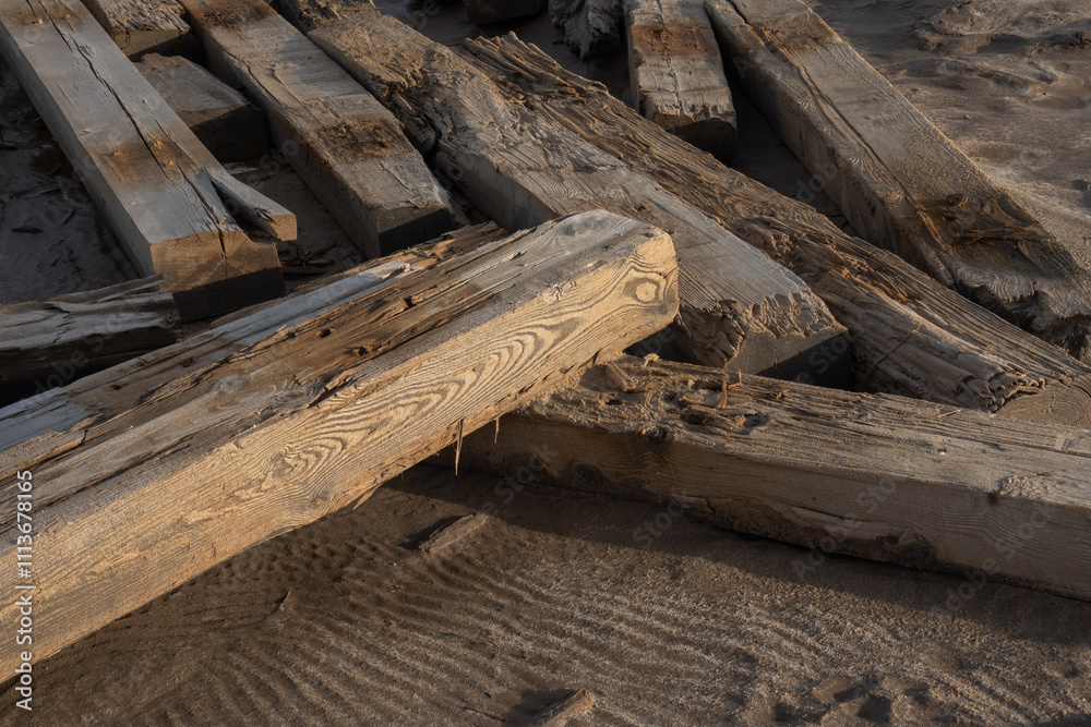 Weathered wooden beams rest on sandy beach. Nature and texture highlighted. Sunset adds warmth. Weathered wooden beams rest on sandy beach. Nature and texture highlighted. Sunset adds warmth.