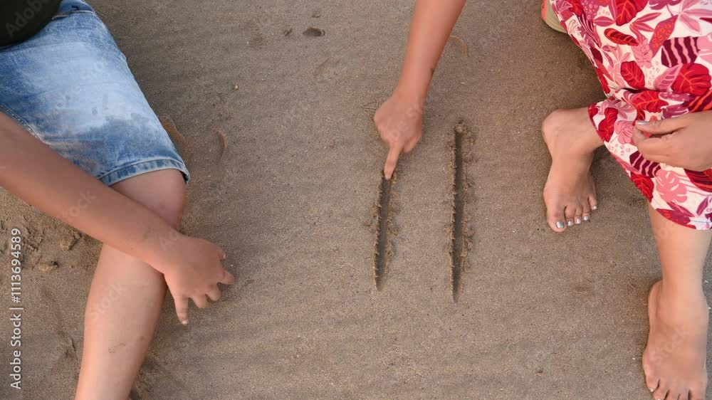 Girl hand drawing tic-tac-toe on the sand.