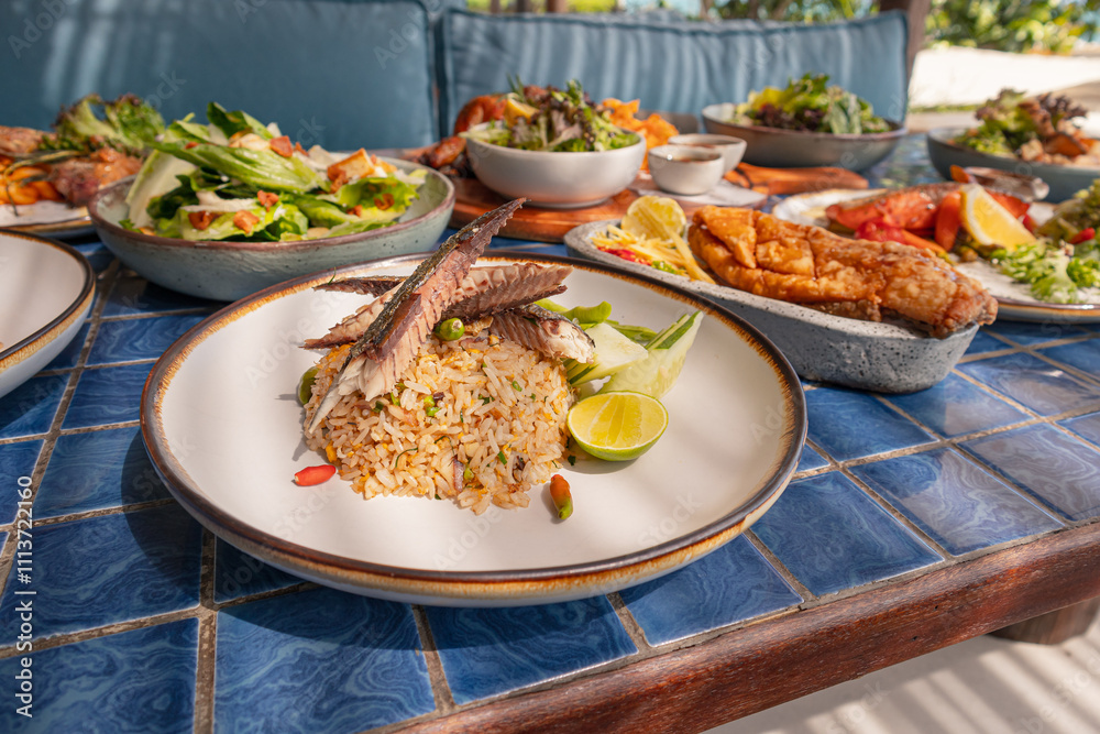 Fried rice with mackerel and include chili, lime and cucumber in plate on blue tiled surface Fried rice with mackerel and include chili, lime and cucumber in plate on blue tiled surface