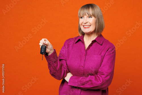 Elderly smiling happy blonde woman 50s years old she wear purple shirt casual clothes hold in hand car key fob keyless system isolated on plain red orange background studio portrait Lifestyle concept photo