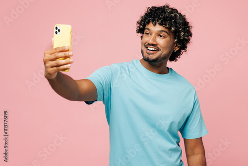 Canvas Print Young Indian man wear blue t-shirt casual clothes doing selfie shot on mobile cell phone post photo on social network isolated on plain pastel light pink background studio portrait