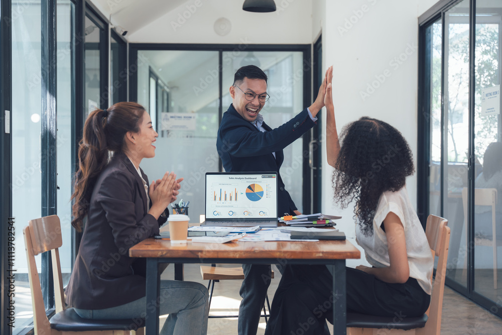 Obraz premium High-Five Success: A diverse team celebrates a business achievement with a celebratory high-five. The image shows three professionals in a modern office setting, reviewing data on a laptop. 