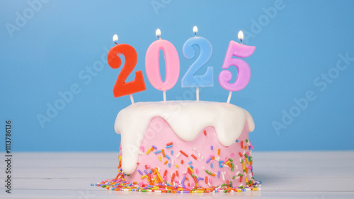 Happy New Year 2025, cute cake with colorful candle number 2025 for new year celebrate party was lit. flame at candlewick sway and flicker with blue background, horizontal photo