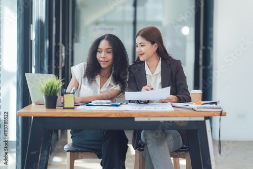 Collaborative Success: Two diverse businesswomen, working together at a modern office desk, showcasing teamwork, communication, and shared goals. 